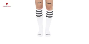 La imagen muestra un par de piernas humanas desde la mitad del muslo hasta los pies. Las piernas llevan puestos unos calcetines blancos que llegan hasta la parte inferior de la pantorrilla. Los calcetines tienen varias rayas negras en la parte superior, justo debajo de la banda elástica. En cada calcetín, cerca del área del tobillo, hay un texto que dice "AMERICAN SHOCKS"