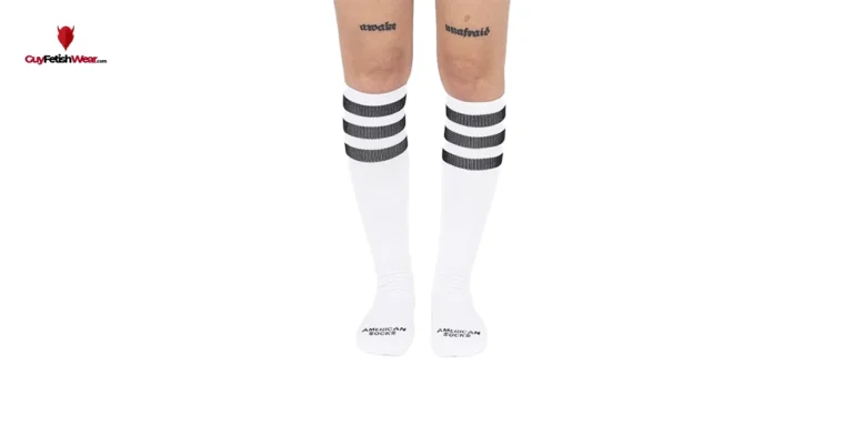 La imagen muestra un par de piernas humanas desde la mitad del muslo hasta los pies. Las piernas llevan puestos unos calcetines blancos que llegan hasta la parte inferior de la pantorrilla. Los calcetines tienen varias rayas negras en la parte superior, justo debajo de la banda elástica. En cada calcetín, cerca del área del tobillo, hay un texto que dice "AMERICAN SHOCKS"
